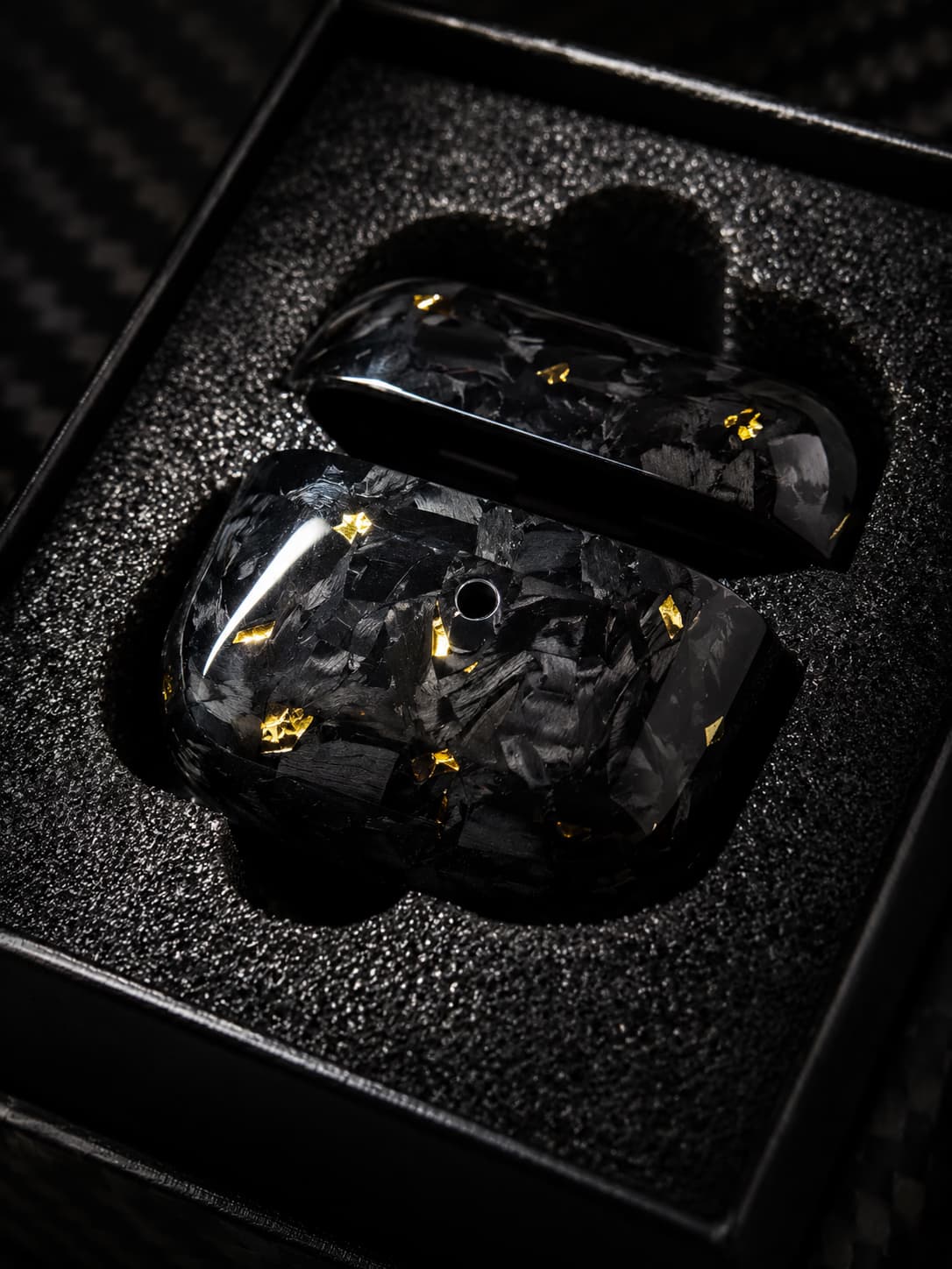 Zweiteiliges Obsidian-Gold-AirPods-Case geöffnet in seiner schwarzen Verpackung